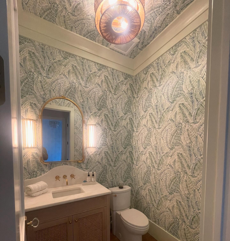 A newly updated powder room with vanity, mirror, light fixtures, and wallpaper by Ravenel Construction Group in Mount Pleasant, SC