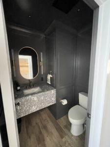 A stylish powder room with a floating vanity, oval mirror, and wall sconces by Abbott Construction LLC in Boxford, MA.