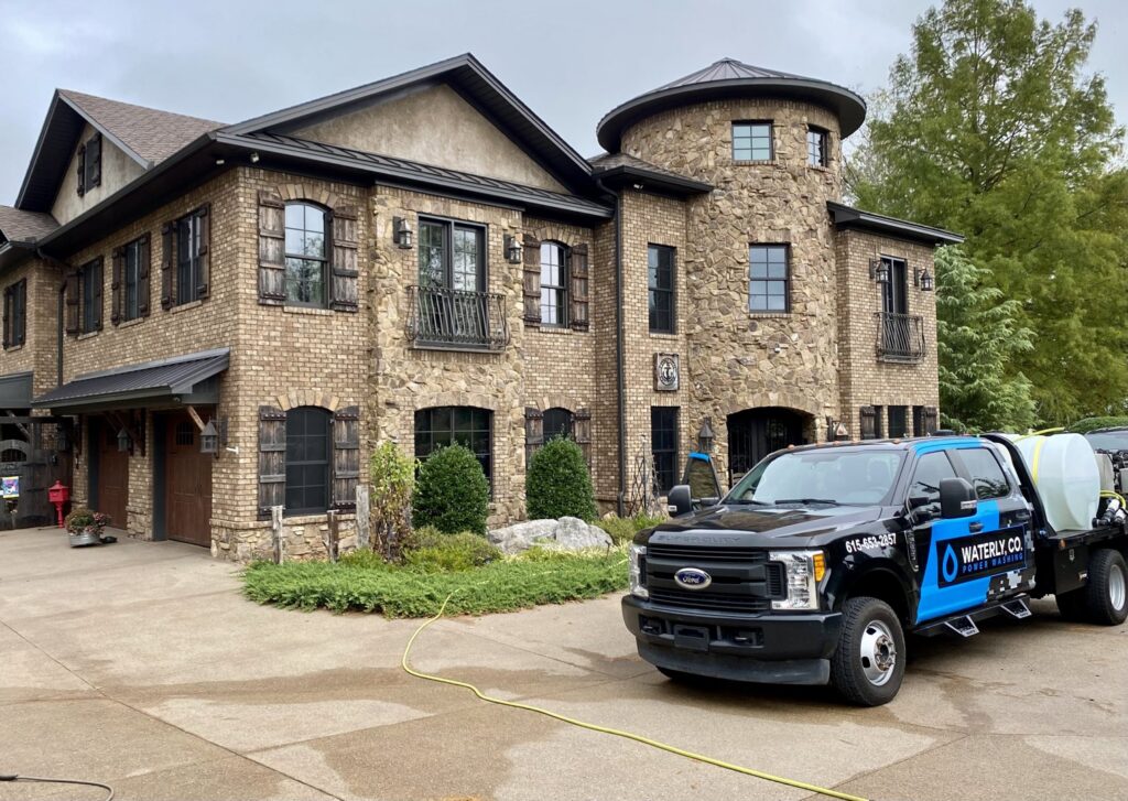 A Waterly, Co. Power Washing technician power washing a brick house exterior in Nashville, TN.