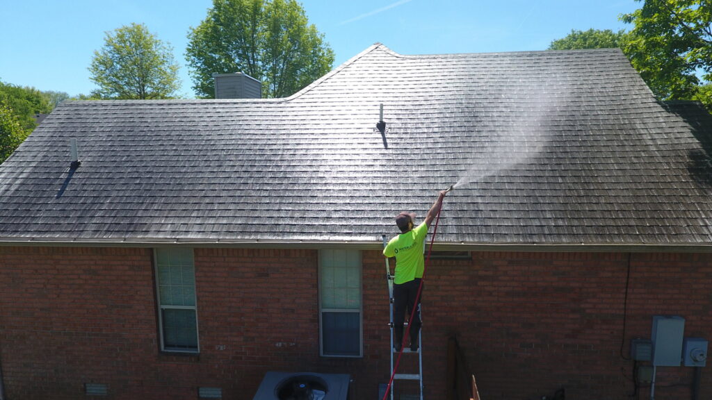 A Waterly, Co. Power Washing technician on a ladder power washing a house roof in Nashville, TN.