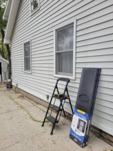 A house exterior with old shutters removed and new shutters in a box, showing preparation for installation by Cedar Valley Maintenance and Handyman Services LLC in Waterloo, IA.