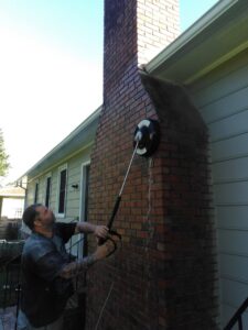 A handyman pressure washing a brick chimney, a service by Holy City Remodel in North Charleston, SC.