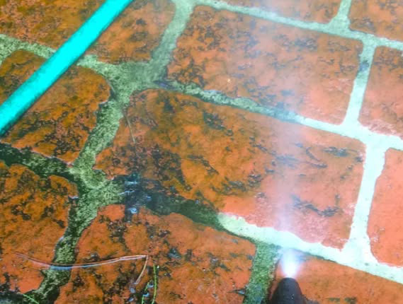 A close-up of a handyman pressure washing a dirty brick patio surface in Greeley, CO, by Northern colorado concrete.