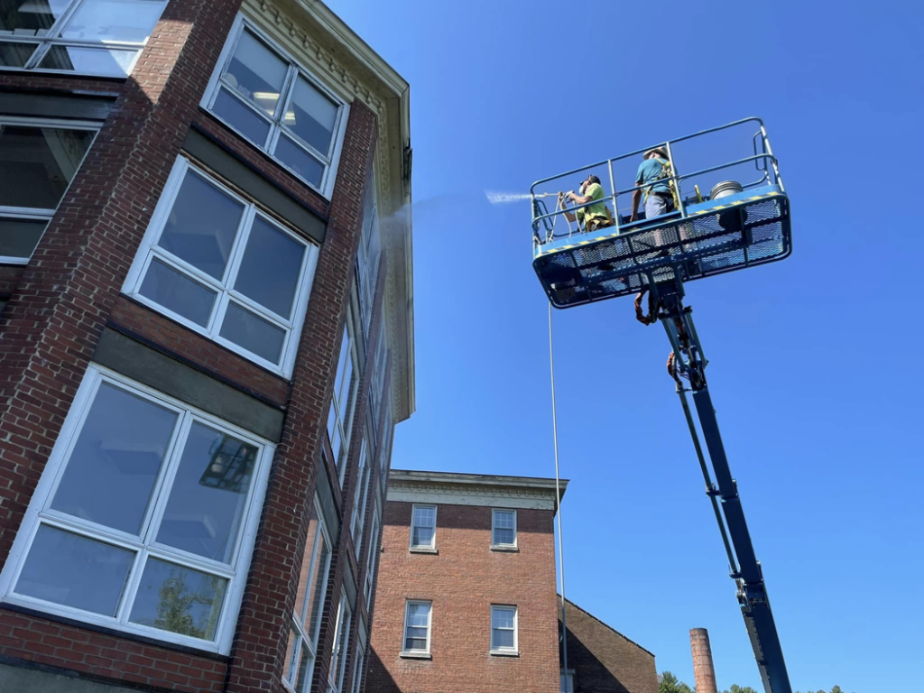 A worker on a boom lift pressure washing the exterior of a brick building for Infinity Maintenance Services, Inc. in Brattleboro, VT.
