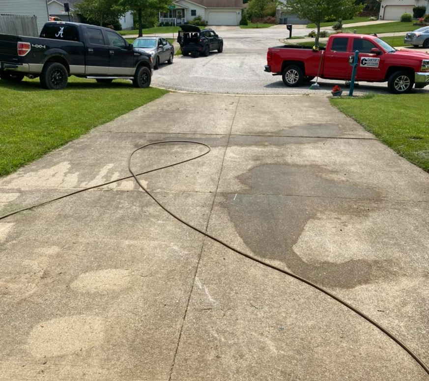 A concrete driveway being pressure washed, showing the cleaning process by Carter's Handyman Service and Remodeling in Bloomington, IN.