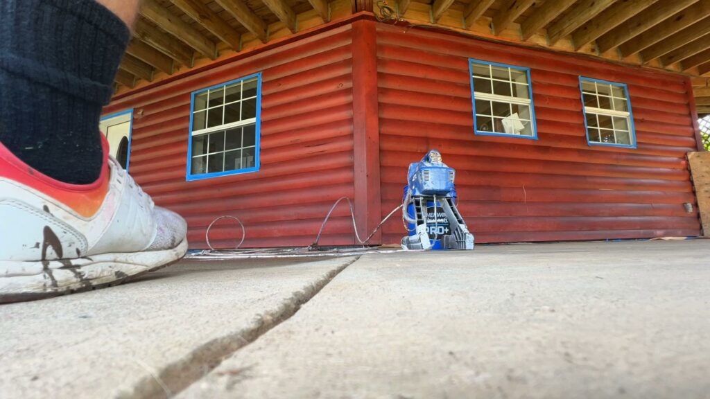 A pressure washer in action on a concrete surface next to a red wooden building, demonstrating exterior cleaning services by OG Renovations in Huntington, WV.
