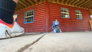 A pressure washer in action on a concrete surface next to a red wooden building, demonstrating exterior cleaning services by OG Renovations in Huntington, WV.