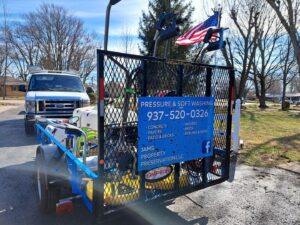 A work van pulling a trailer with pressure washing equipment and a service advertisement for JAMS Property Preservation LLC in Dayton, OH.