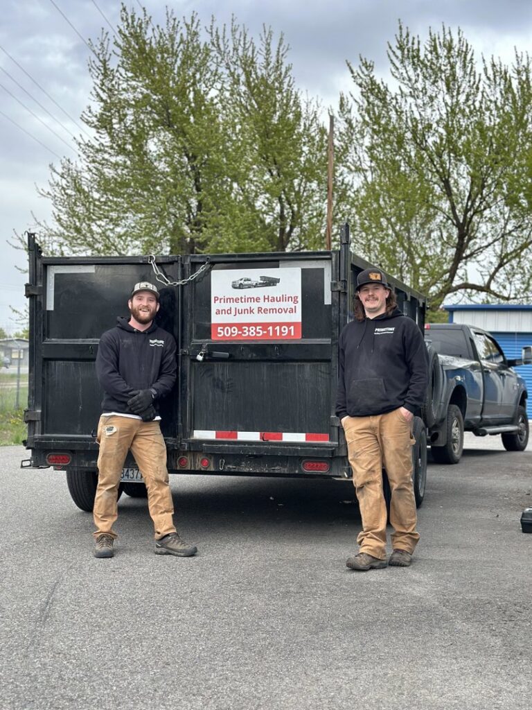 Two Primetime Hauling and Junk Removal team members standing proudly in front of their dump trailer in Spokane, WA.