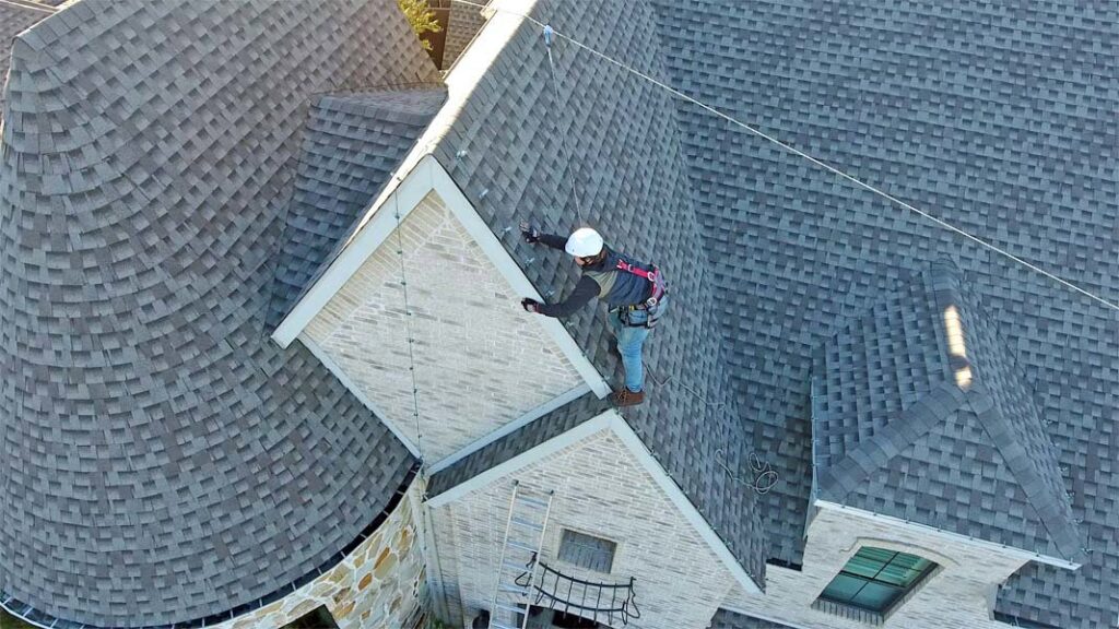 An aerial view of a professional holiday light installer on a roof, wearing a helmet and harness, for Ohio Holiday Lighting in Akron, OH.