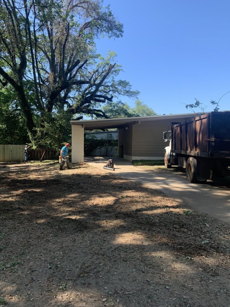 A cleared residential property with a worker and dump truck after tree service by Clifford & Sons Tree Service in Mobile, AL