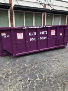 A purple All In Waste LLC dumpster parked outside a commercial building in Greenville, SC.