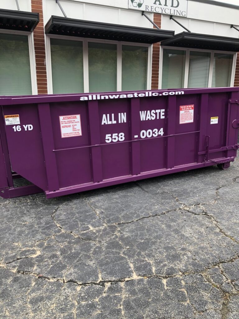 A purple All In Waste LLC dumpster parked outside a commercial building in Greenville, SC.