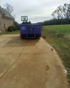 A purple All In Waste LLC dumpster placed on a residential driveway in Greenville, SC.