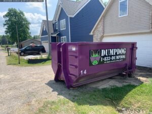 A purple DumpDog dumpster placed in a residential driveway for junk removal services in Flint, MI.