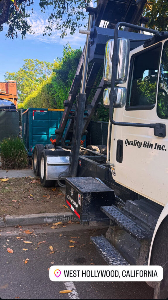 A Quality Bin Inc. truck delivering a dumpster on a residential street in West Hollywood, Los Angeles, CA.