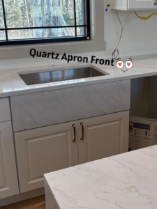 A modern kitchen with a newly installed quartz apron front sink and white cabinets by Slater Cabinets and More in Springfield, MO.
