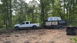 A Quick Lift Junk Removal truck and branded trailer loaded with items in a wooded area in Hagerstown, MD.