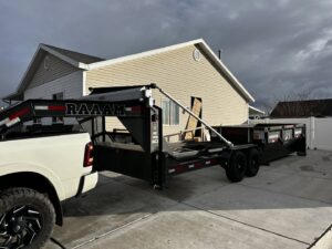 A RAAAM Dumpster Rentals truck delivering a roll-off dumpster to a residential driveway in Salt Lake City, UT.