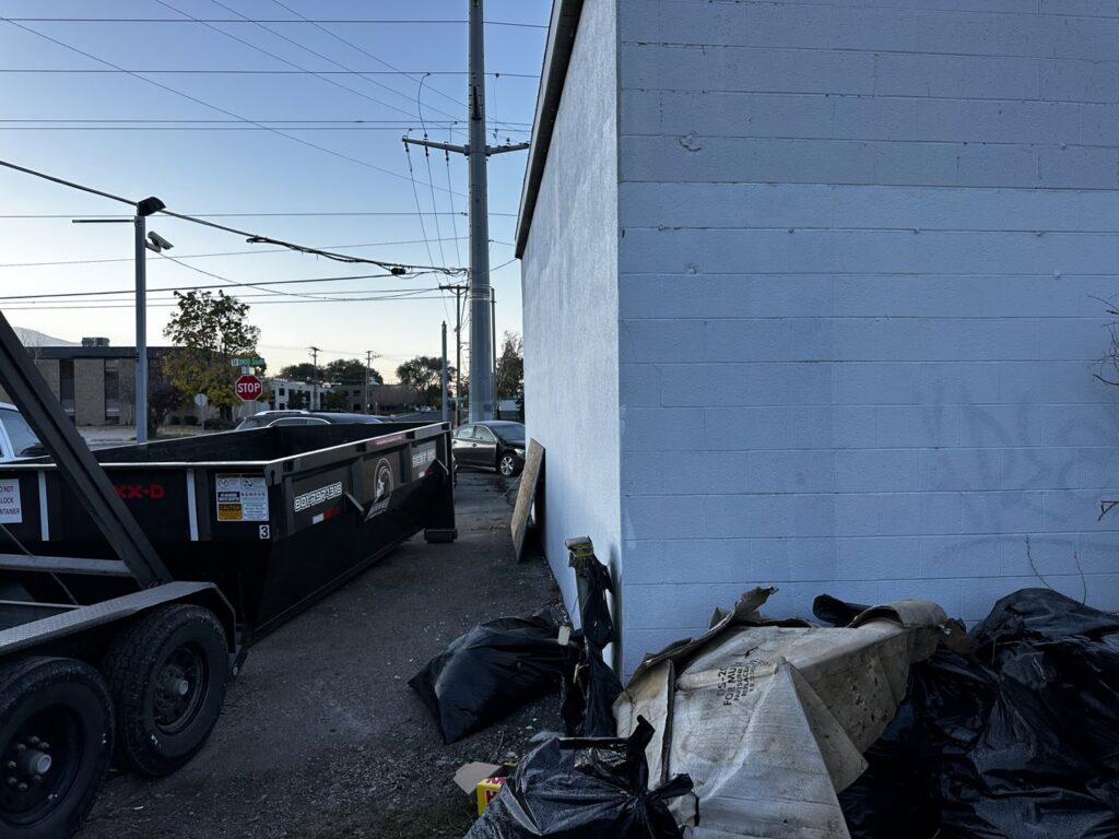 A RAAAM Dumpster Rentals dumpster placed next to a building with debris on the ground, ready for junk removal in Salt Lake City, UT.
