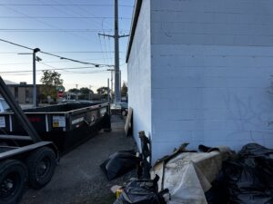 A RAAAM Dumpster Rentals dumpster placed next to a building with debris on the ground, ready for junk removal in Salt Lake City, UT.