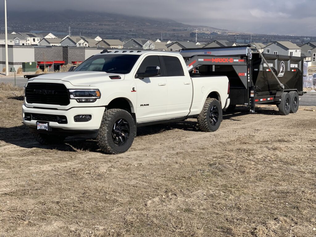 A RAAAM Dumpster Rentals truck pulling a roll-off dumpster trailer at a construction site in Salt Lake City, UT.