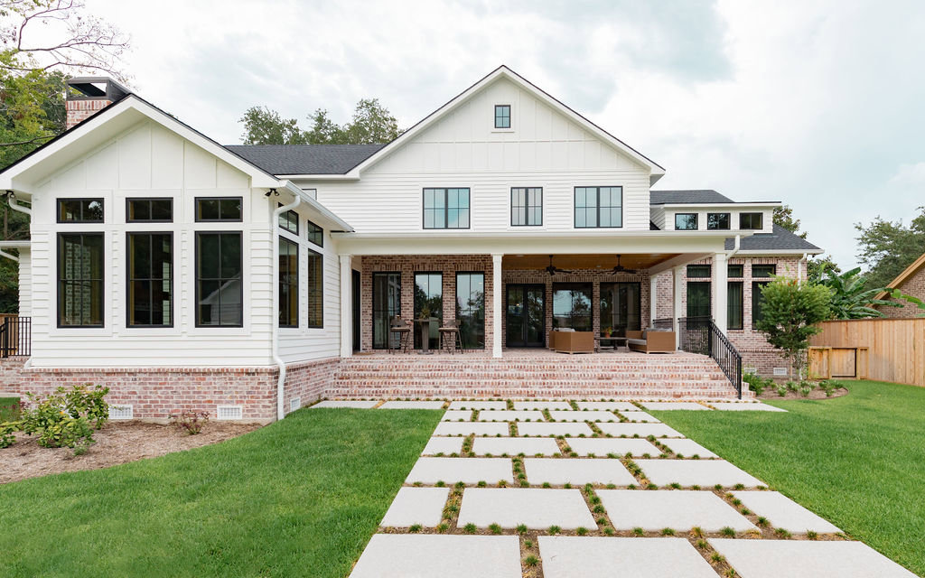 The rear exterior of a large white modern farmhouse-style home with a brick patio by Stone Acorn Builders in Bellaire, TX.