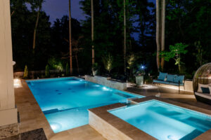 A stunning rectangular pool and hot tub illuminated at night by Extreme Pools Renovation in Raleigh, NC.