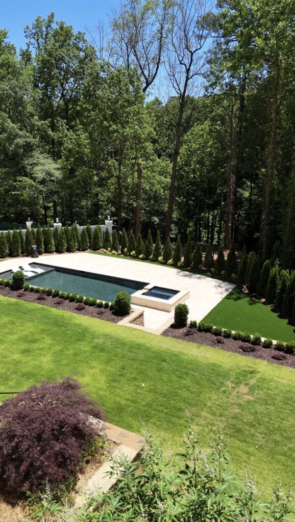 A modern rectangular swimming pool and spa surrounded by artificial turf and manicured hedges, a project by Picasso Poolscapes in Johns Creek, GA.