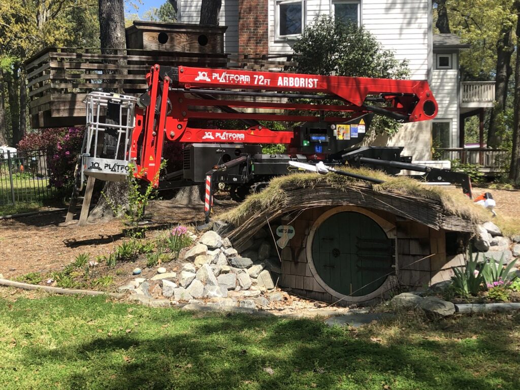 A red JLG Platform 72ft Arborist lift positioned in a residential yard for tree work by Scott Lanes Tree Service in Chesapeake, VA.