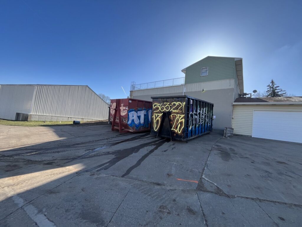 Red and blue roll-off dumpsters from AT Disposal parked at a job site in Dewitt, IA.