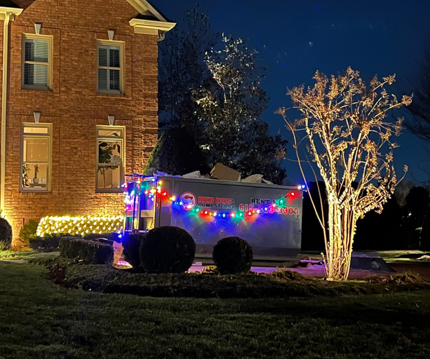 A Red Dog Dumpsters junk removal dumpster filled with debris, decorated with lights, outside a residential home in Nashville, TN