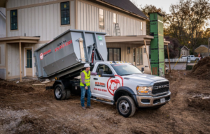 A Red Dog Dumpsters truck deploying a roll-off dumpster at a construction site with a worker in Nashville, TN
