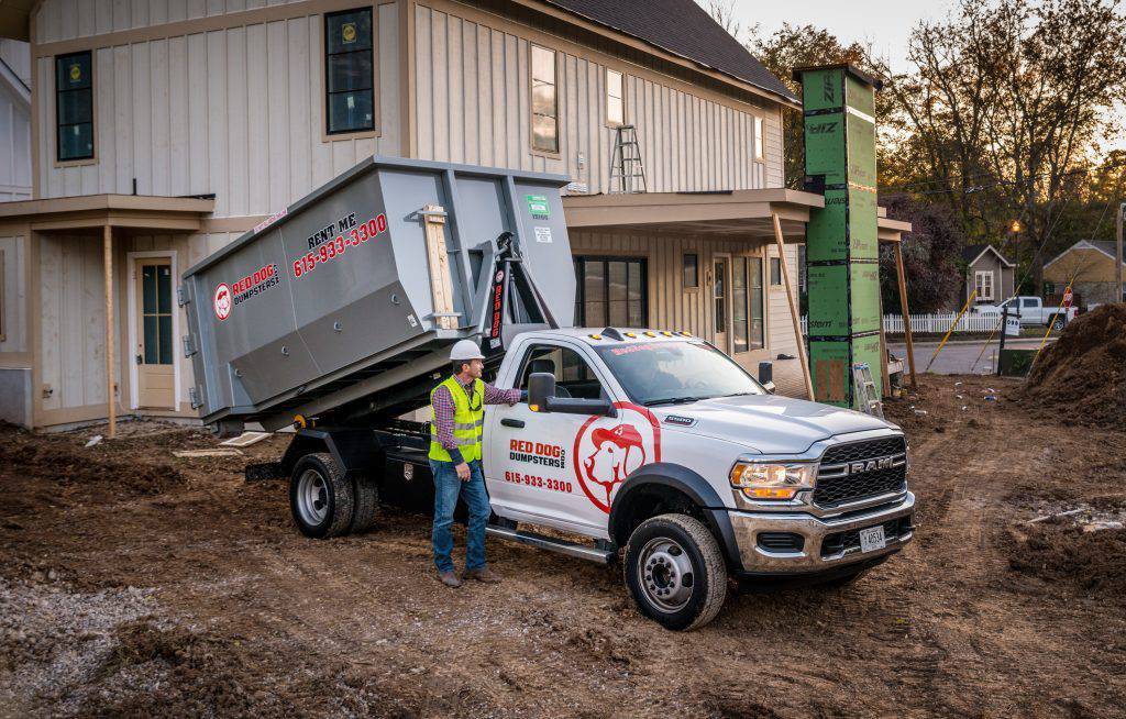 A Red Dog Dumpsters truck deploying a roll-off dumpster at a construction site with a worker in Nashville, TN