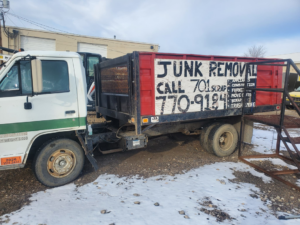 A red dump truck with "JUNK REMOVAL" painted on its side, used by 701 Scrap for hauling in Williston, ND.
