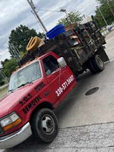 A red Sos Junk Removal dump truck loaded with various items and debris in Akron, OH.