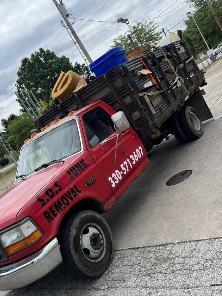 A red Sos Junk Removal dump truck loaded with various items and debris in Akron, OH.