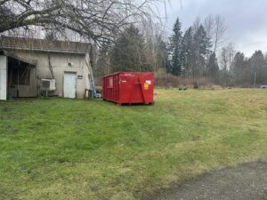A red dumpster from Cascade Container and Recycling placed in a grassy field next to a building in Seattle, WA.