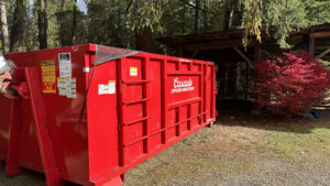A red dumpster from Cascade Container and Recycling placed in a wooded area next to a wooden structure in Seattle, WA.