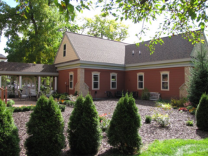 A beautifully maintained red house exterior with a covered patio and lush landscaping by Ankeny Builders L.L.C. in Eau Claire, WI.