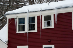 A red house exterior with snow and icicles on the roof and gutters, indicating potential repair needs from Neville's Inc. in Green Bay, WI.