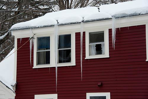 A red house exterior with snow and icicles on the roof and gutters, indicating potential repair needs from Neville's Inc. in Green Bay, WI.