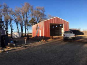 A red metal barn under construction with a worker on a ladder, built by K&K Construction LLC in Enid, OK