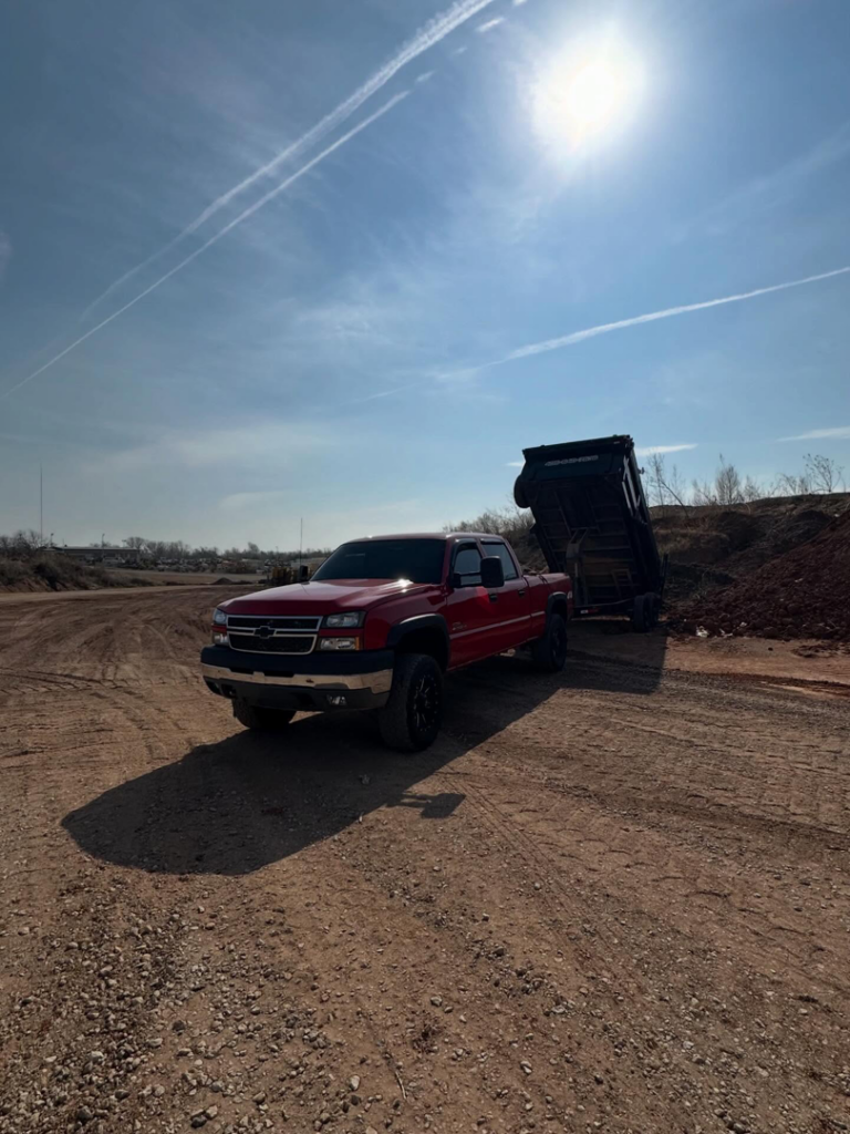 A red pickup truck with a dump trailer raised, actively dumping material for Ricky's Dump Truck in Oklahoma City, OK.
