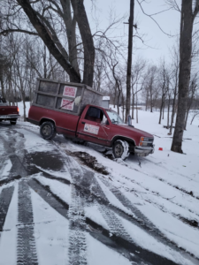 A red pickup truck with a Newell Sanitation junk removal container on a snowy road in Waco, KY.
