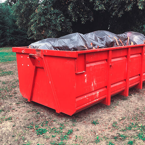 A red roll-off dumpster filled with junk and trash bags, ready for removal by ABC Waste of Savannah, Inc. in Savannah, GA.