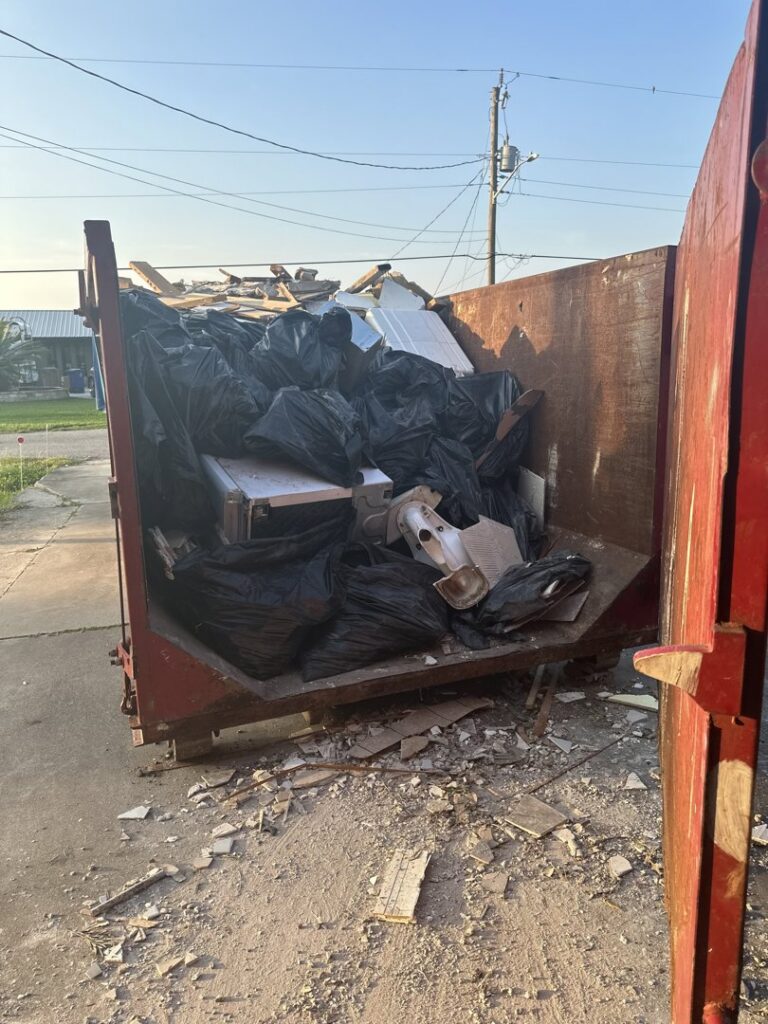 A red roll-off dumpster filled with black trash bags and debris, showing a completed junk removal job by Coast to Coast Disposal in Orlando, FL.