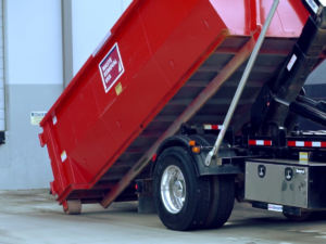 A red roll-off dumpster being loaded onto a truck for general junk removal by Waste Removal USA in Austin, TX