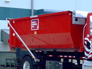 A red roll-off dumpster fully loaded on a Waste Removal USA truck, ready for general junk removal in Austin, TX