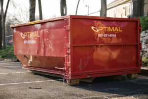 A large red roll-off dumpster from Optimal Roll-Offs parked in a lot in Papillion, NE.